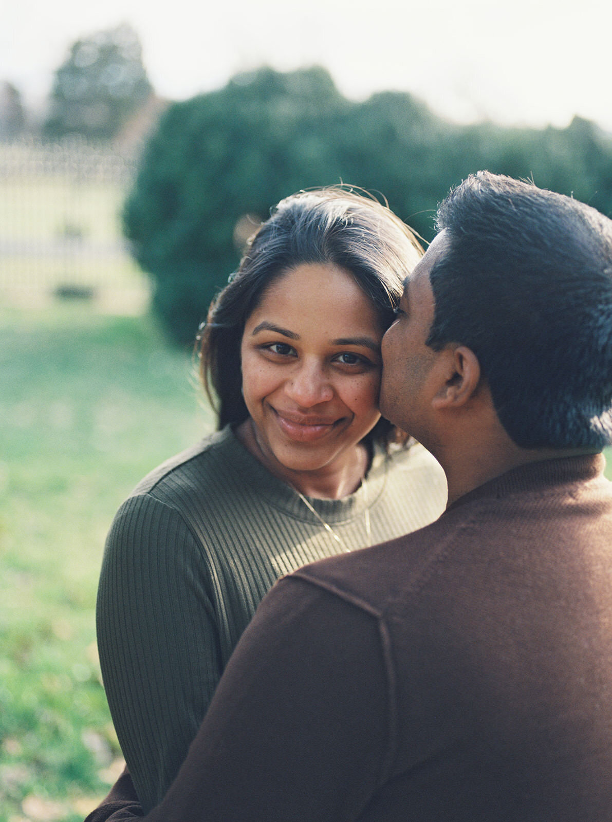 Tender outdoor couple's maternity portrait, with the father-to-be kissing the mother-to-be on the cheek.