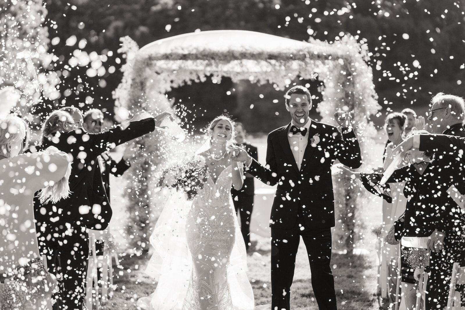 A bride and groom celebrate as they walk down the aisle and their guests throw rose petals into the air