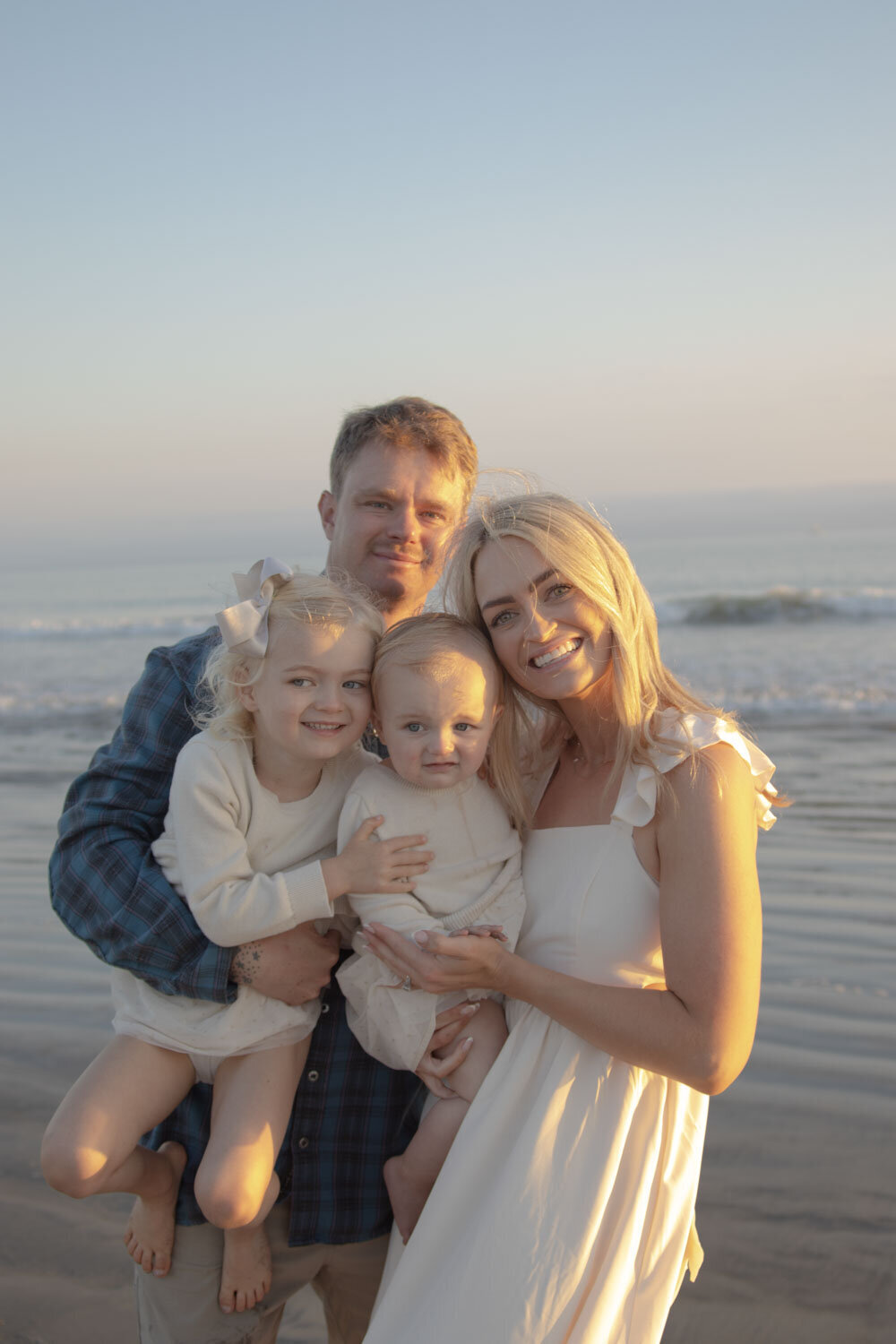 Family of four smiling on the beach during sunset