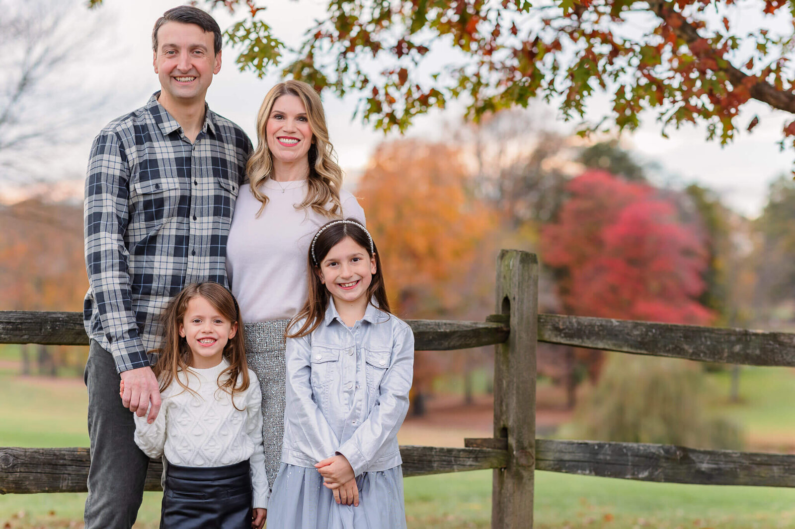 A NOVA family standing at a fence with fall foliage behind them.
