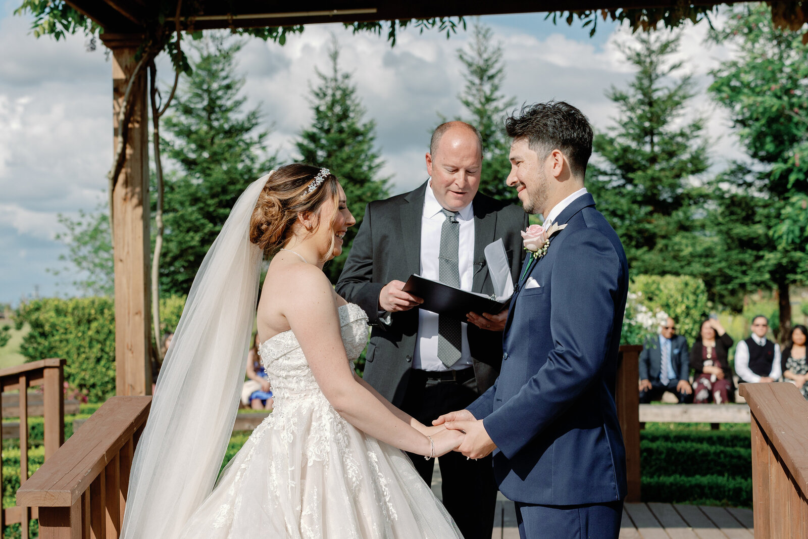 sacramento wedding photographer captures bride and groom holding hands as their officiant marries them in a pergola at Wolfe Heights wedding venue for outdoor Bay Area wedding