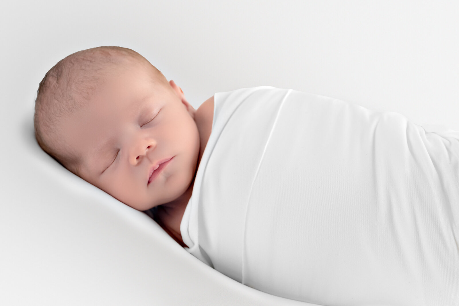 A newborn baby wrapped in white laying on his side for a newborn photo session in Huntsville