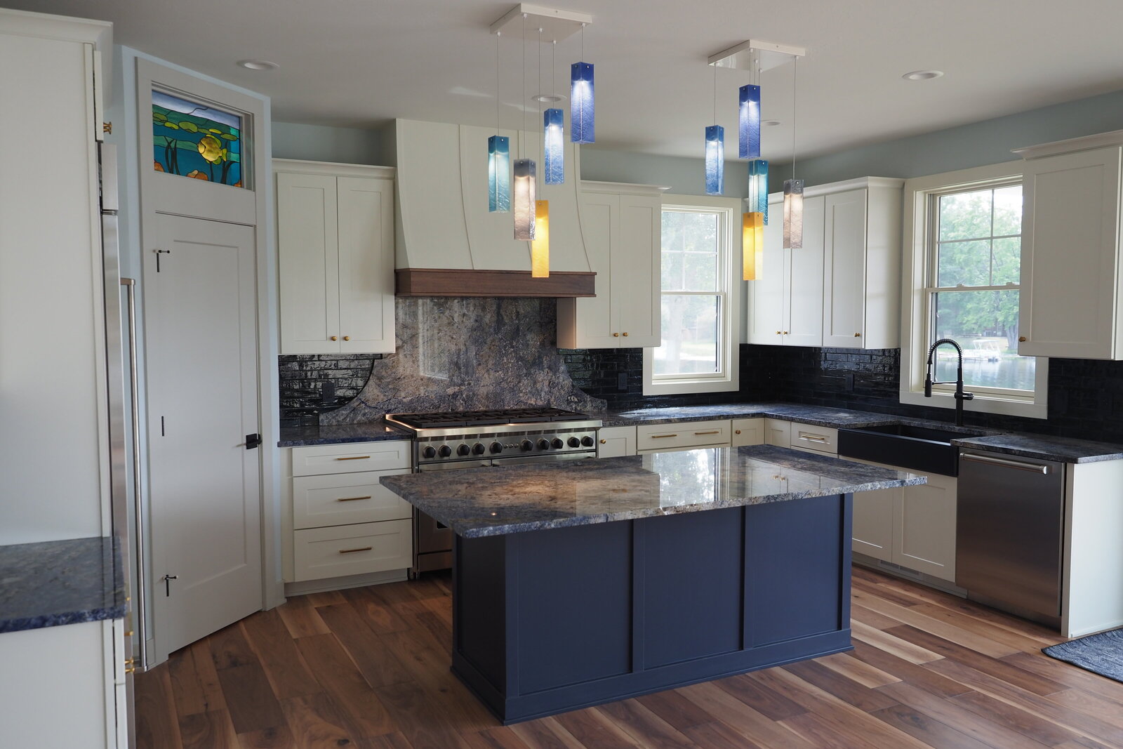 Kitchen with blue island and colorful pendant fixtures above it.