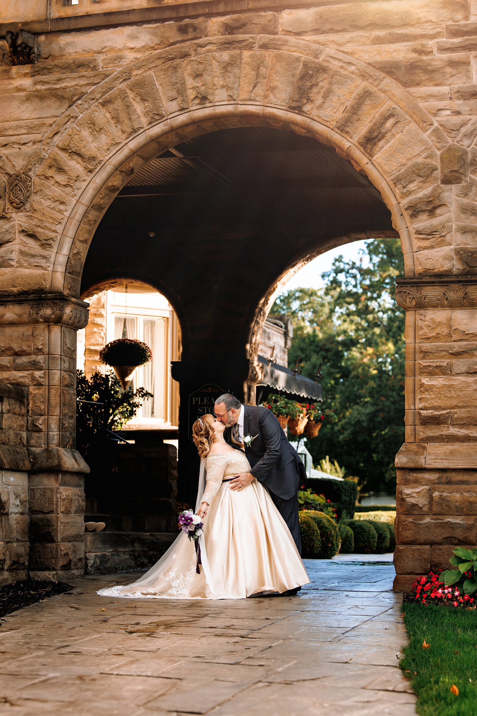 Groom dips bride under a beautiful stone archway  at Buhl's Mansion