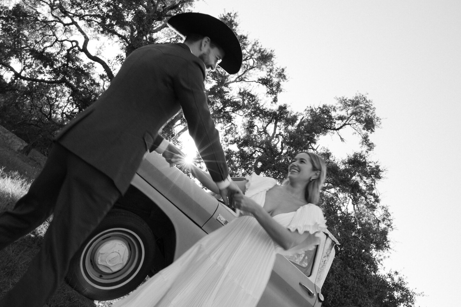 A groom wearing a cowboy hat and dancing with his bride with a truck in the background. 
