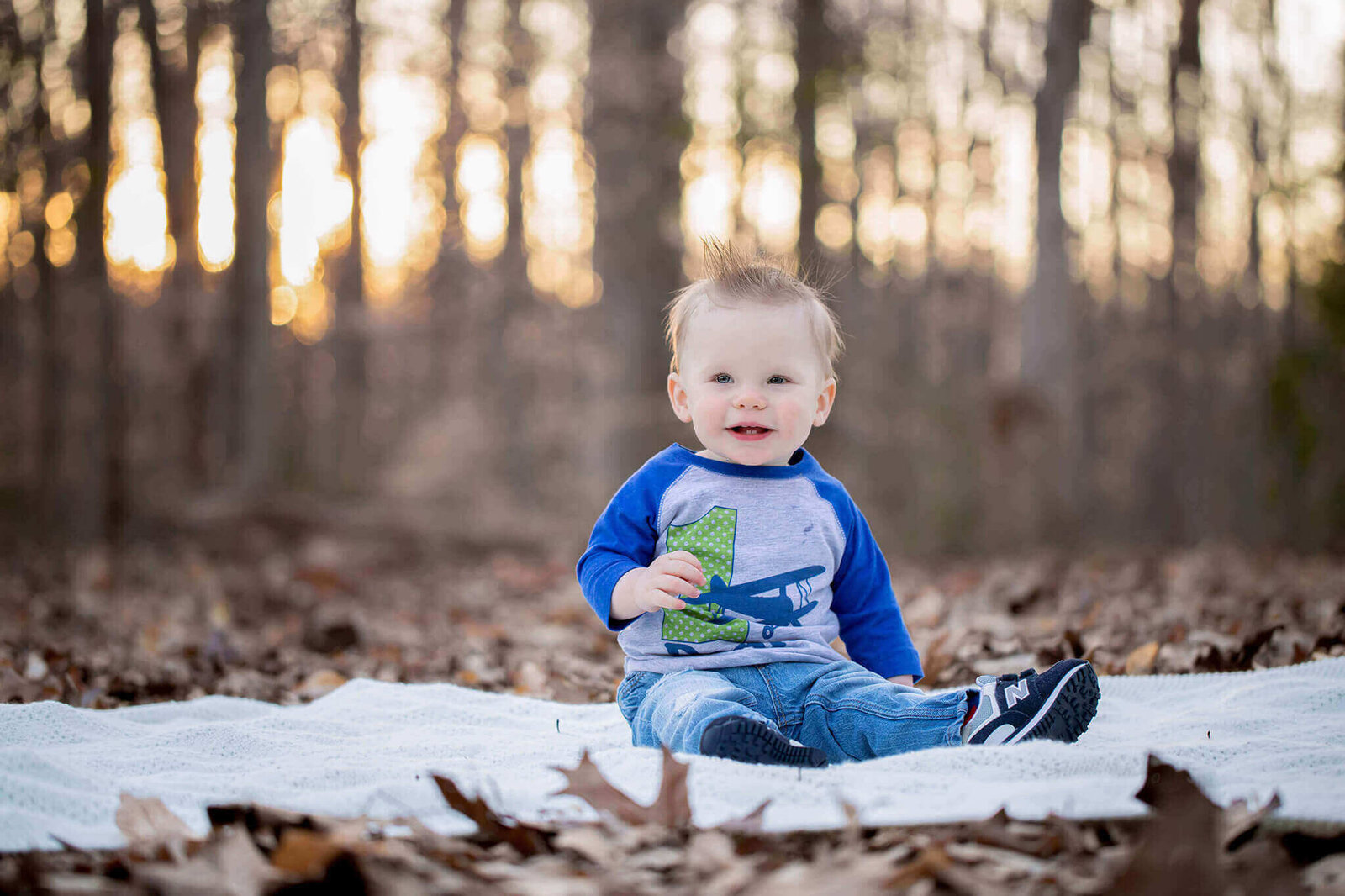 A little boy sitting on a blanket and holding a toy airplane.