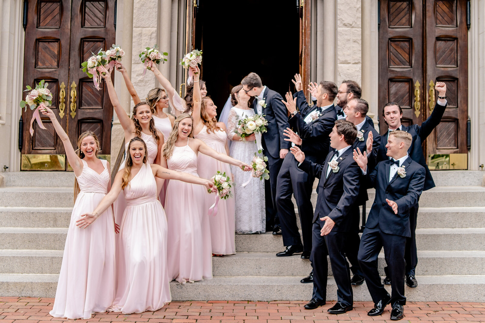 A wedding party cheering as the bride and groom share a kiss on the front steps after a wedding at the Basilica of Saint Mary in Alexandria Virginia