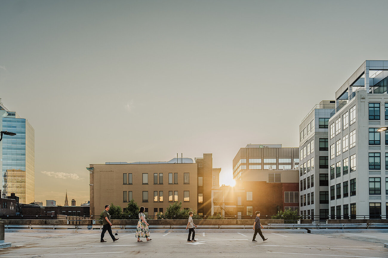 family with two sons walks across a parking garage roof at sunset in the city