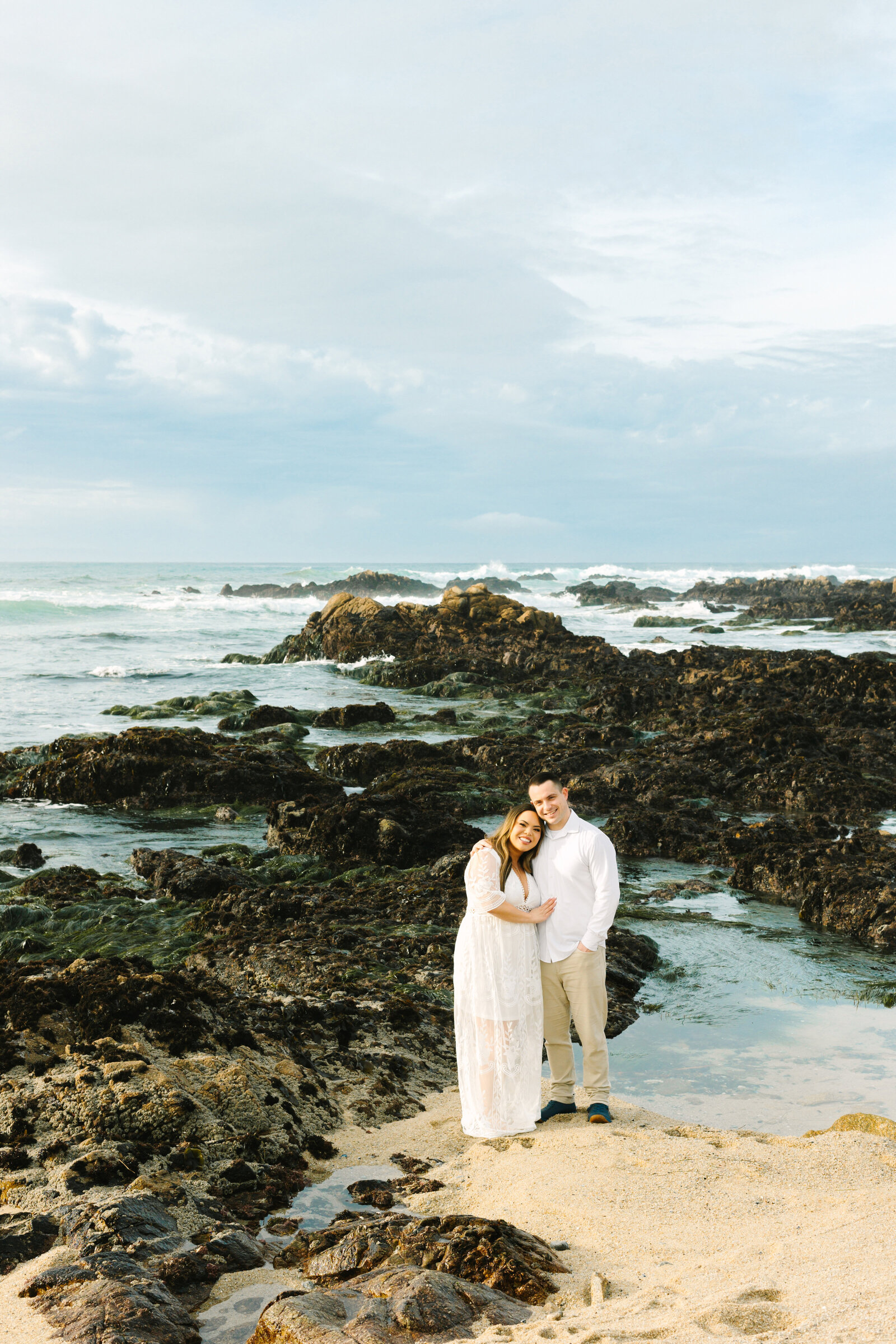 An engaged man and woman take photos on the beach in Pacific Grove, Monterey, California near Big Sur.