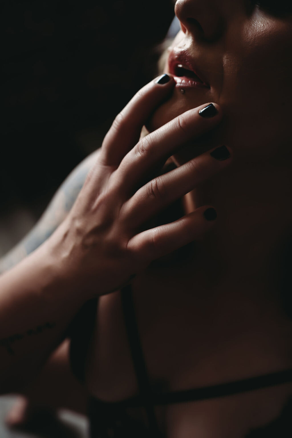 close up boudoir image of woman in black lingerie showing breasts with hand on lips