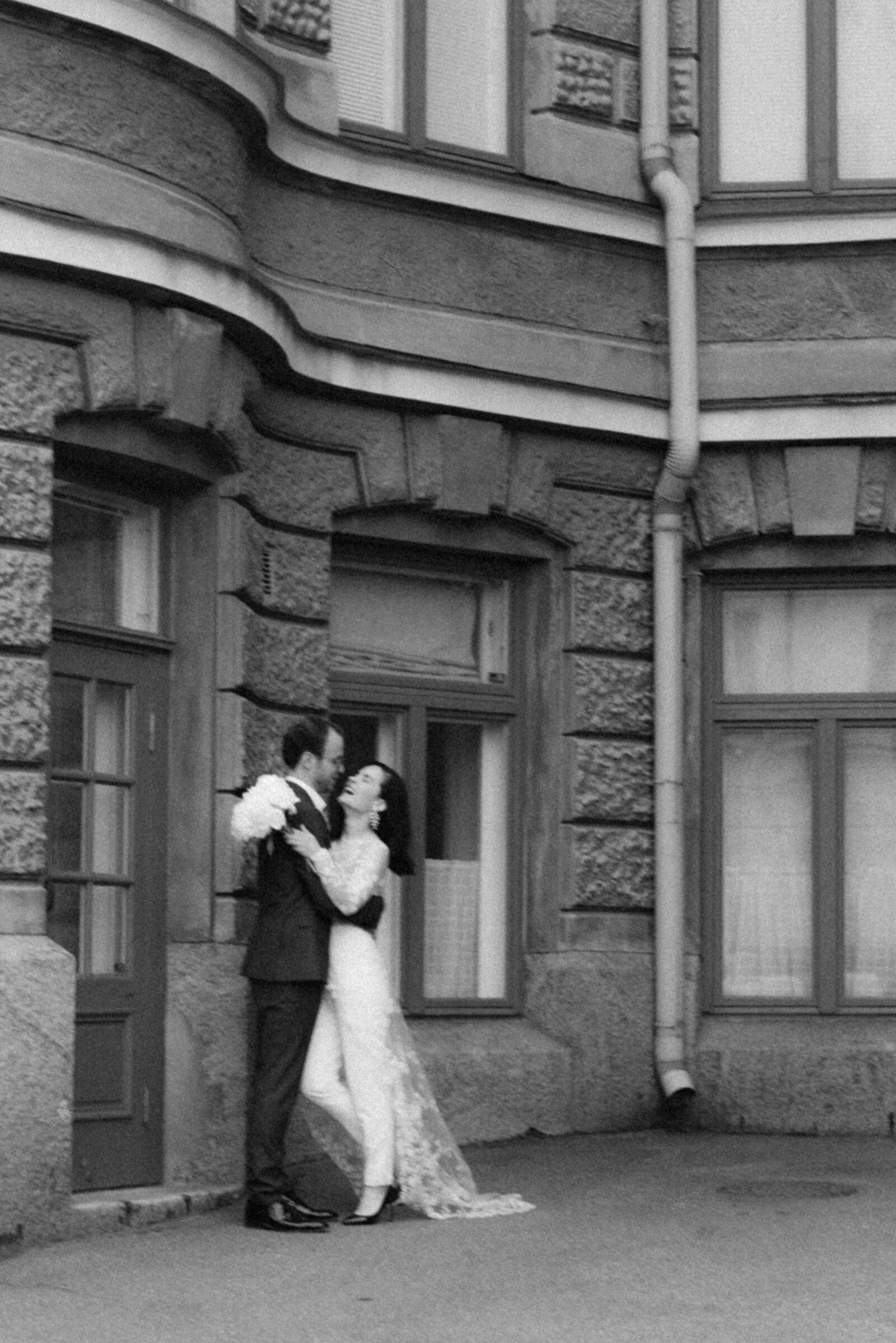 Hääpari seisoo ja nauraa rakennuksen edessä. Morsiamella on tyylikäs häähaalari. hääkuvaaja Hannika Gabrielssonin ikuistama kuva.