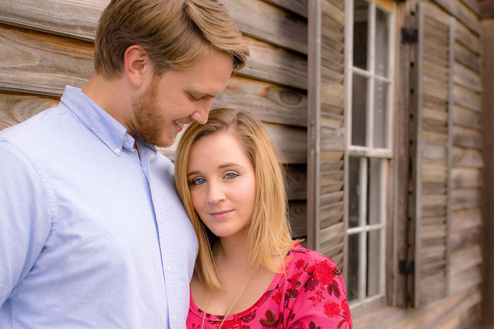 A couple standing in front of an old wooden house.
