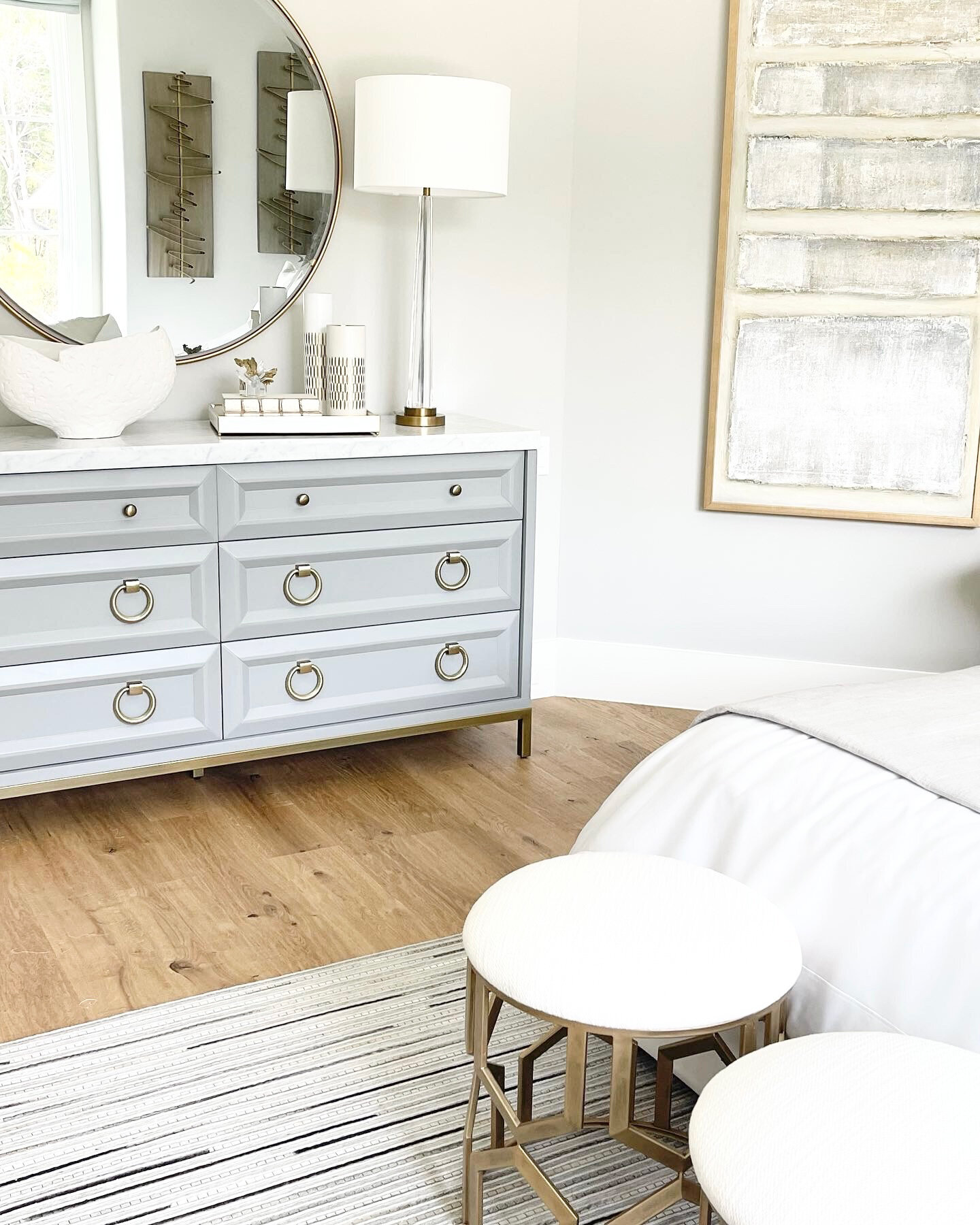 Interior Design Frisco TX project for the main bedroom, featuring a table with elegant lamps, a circular mirror, and two small white tables next to the bed.