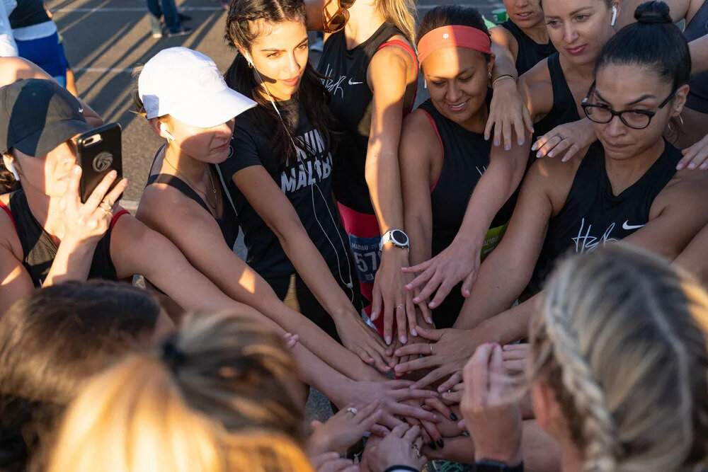 HER Sports Club members joining hands in a group huddle before training.