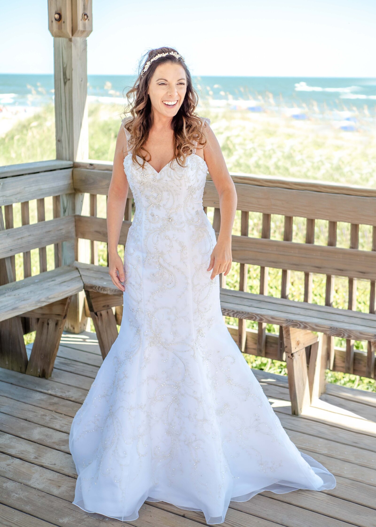 Joyful bride smiling in her stunning wedding gown on a beach deck, with the ocean in the background, captured in Ocean Isle Beach, North Carolina.