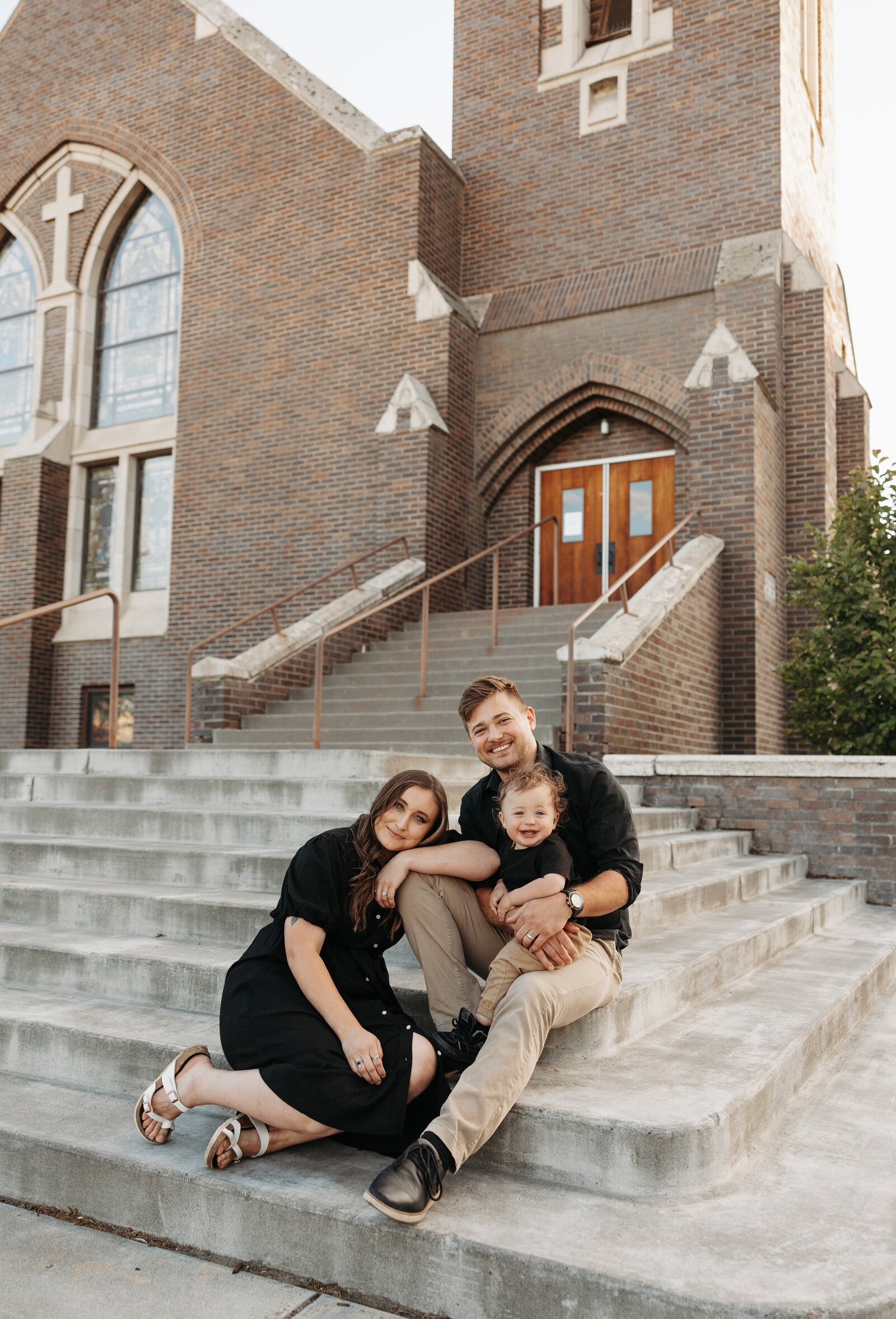 Family of 3 sits on the steps of a church