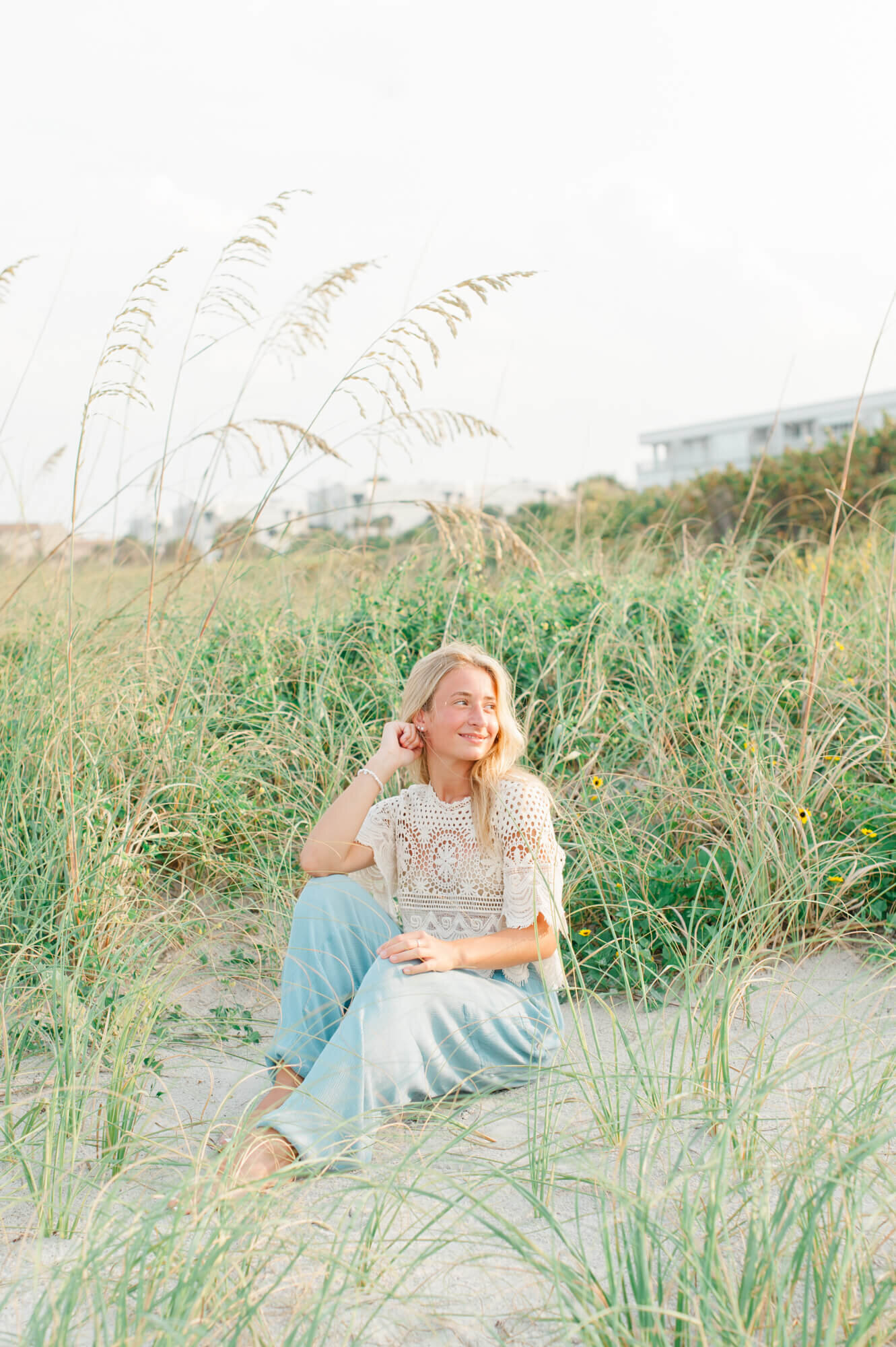 Blonde senior girl sitting in the dunes during her photos at the beach
