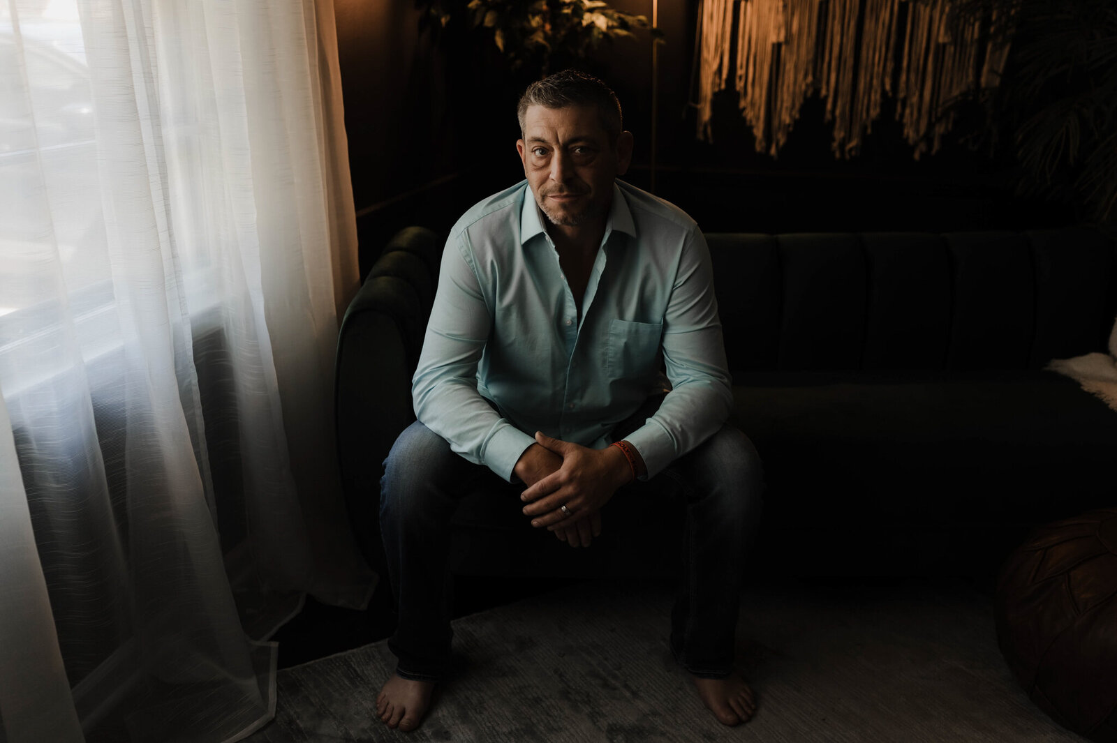 Man in jeans and blue shirt sitting in a chair under a window