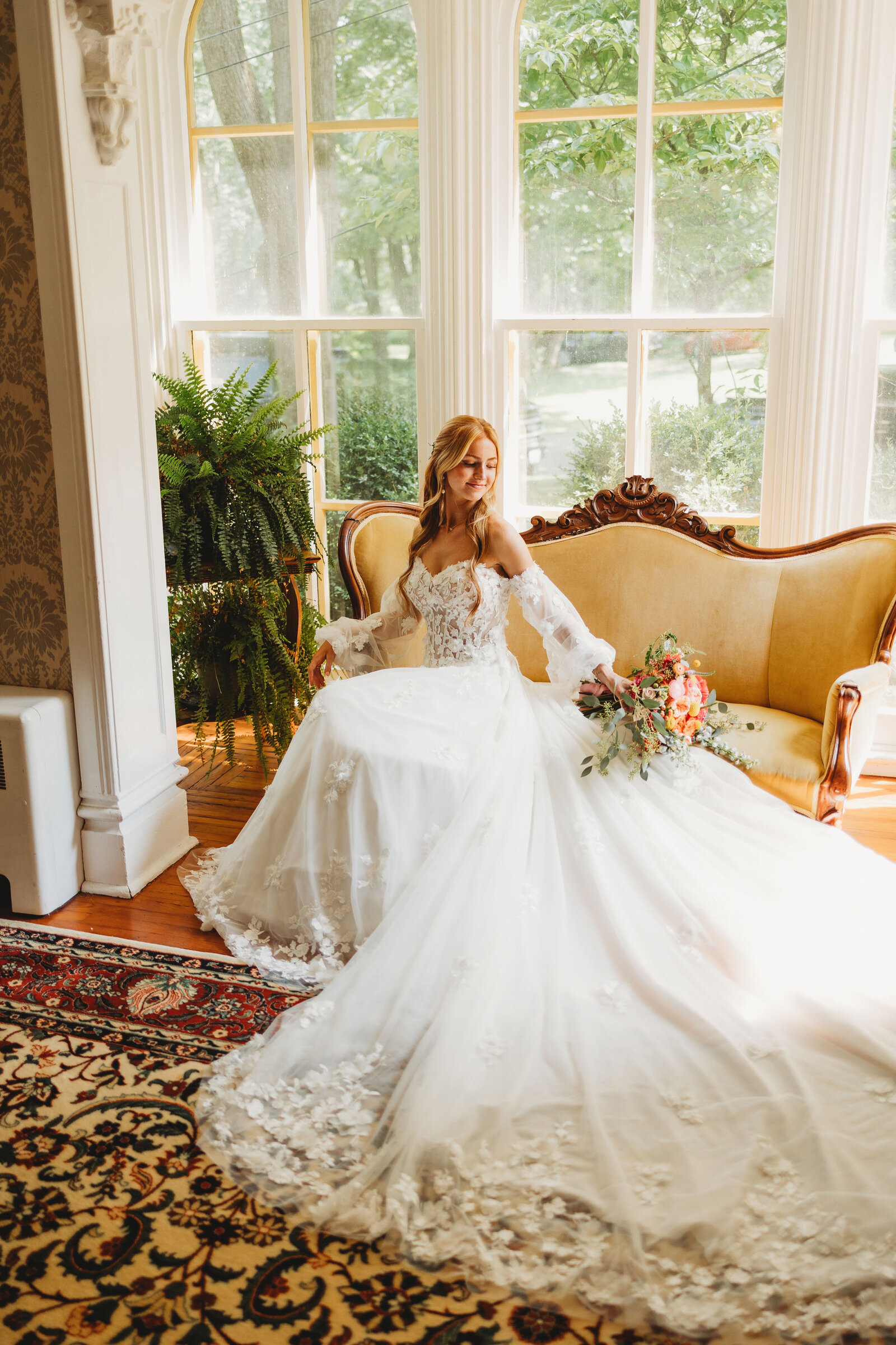 Stunning bride sits on antique couch with her beautiful wedding dressed spread out around her 
