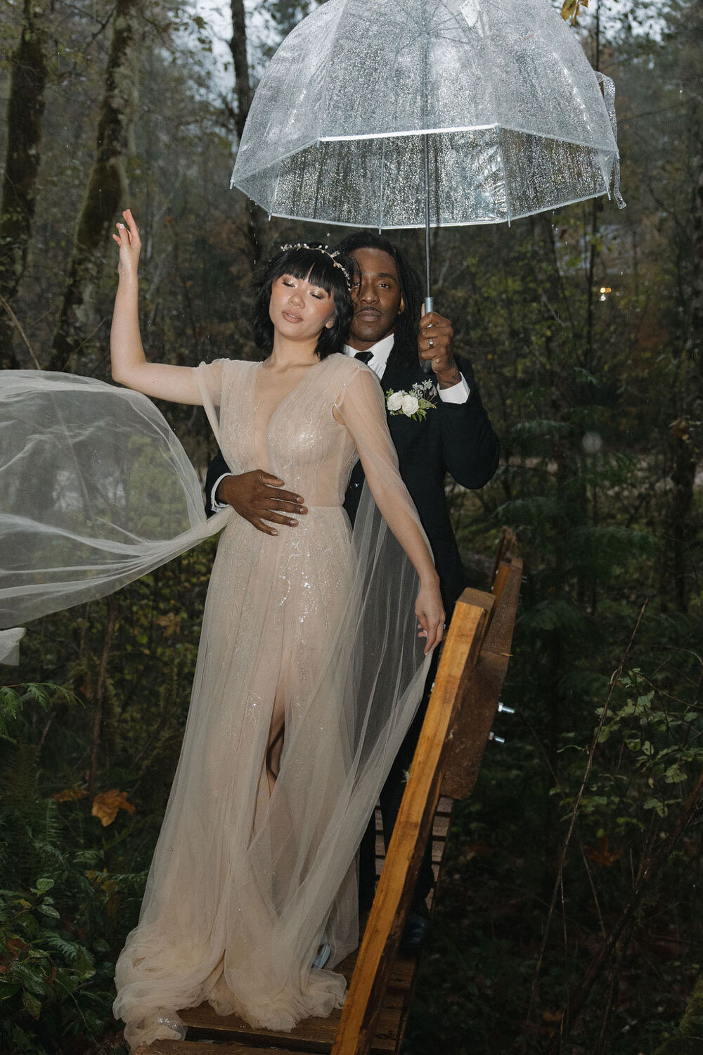 Bride and groom under a clear umbrella in a forest setting