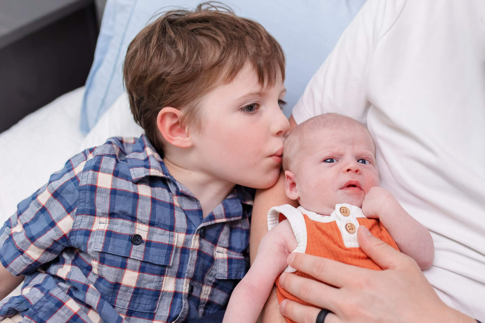 A big brother kissing his newborn brother on the head.