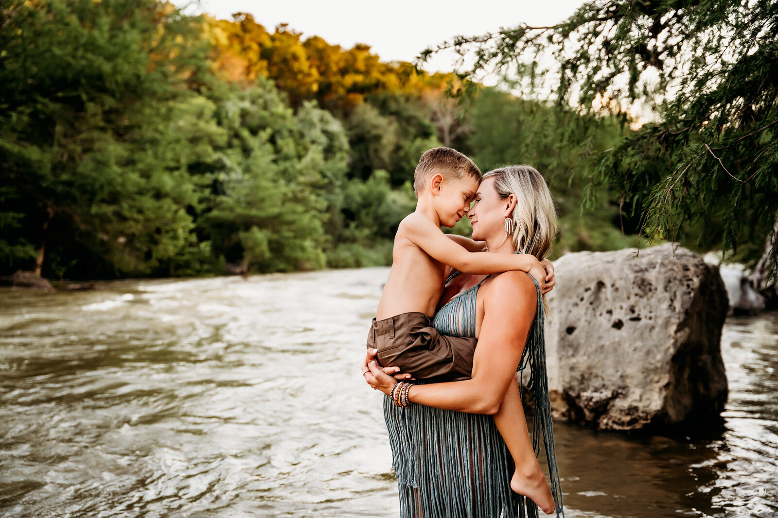 Maternity Photographer, a pregnant mother holds her older son near the river in the forest