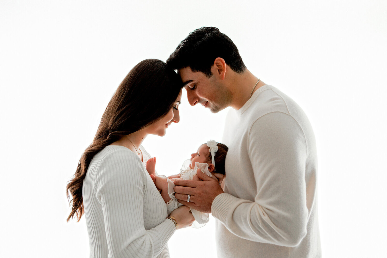 new parents holding newborn baby girl in an all whote backlit iage. mom and dad heads together, baby girl in the middle, fresno, clovis, california, photography