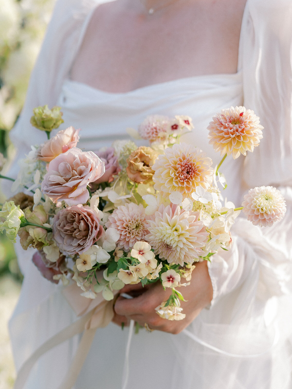 Bridal bouquet including blush garden roses, taupe garden roses, blush dahlias, peach dahlias, peach lisianthus, phlox, and white hydrangea.