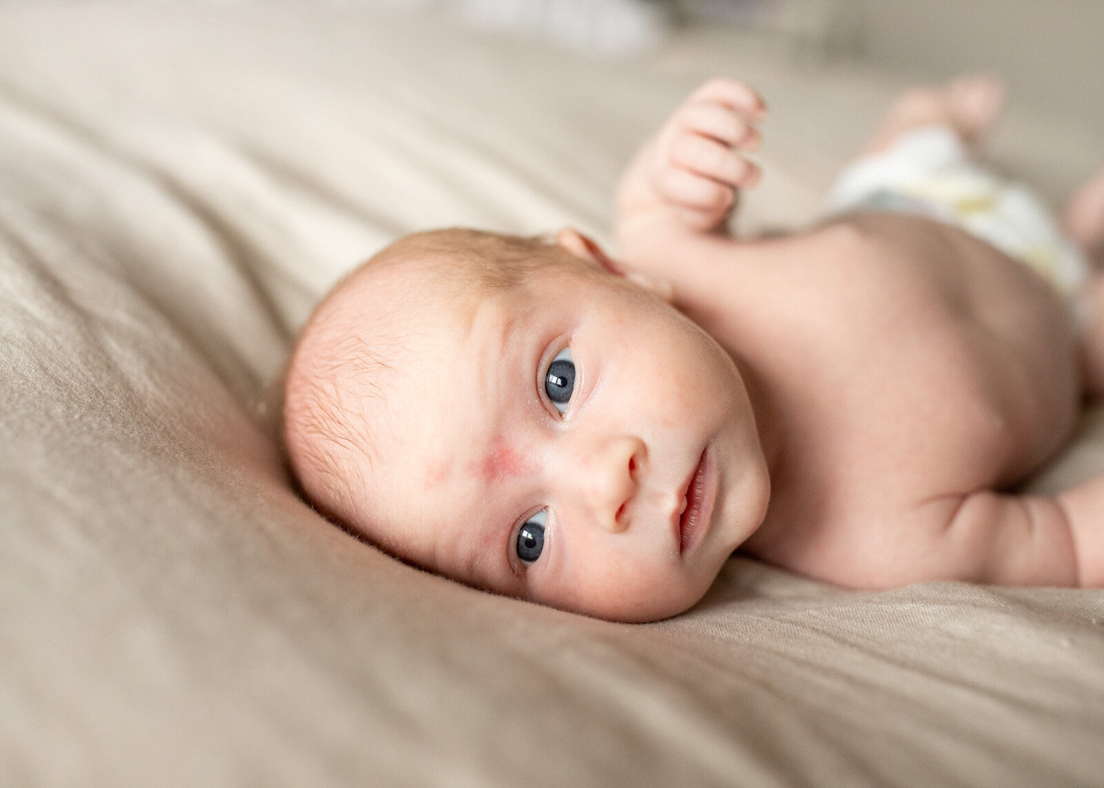 Newborn baby laying on neutral colored bedding.