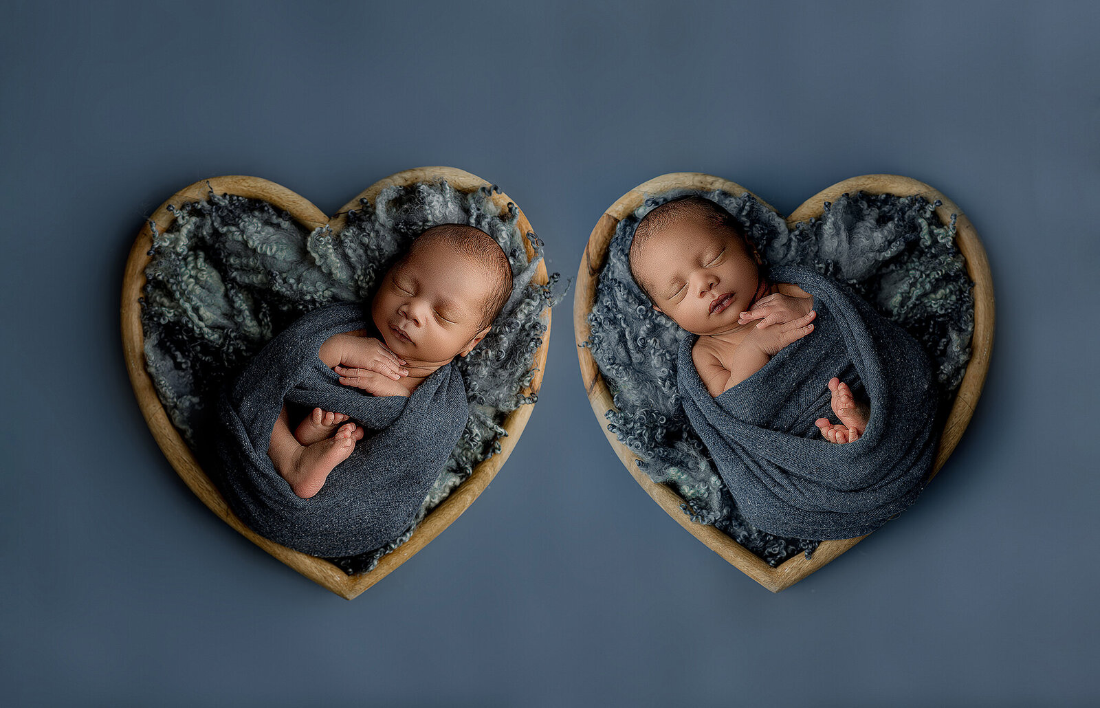 twin newborn boys each in a heart shaped box wrapped in a blue wrap