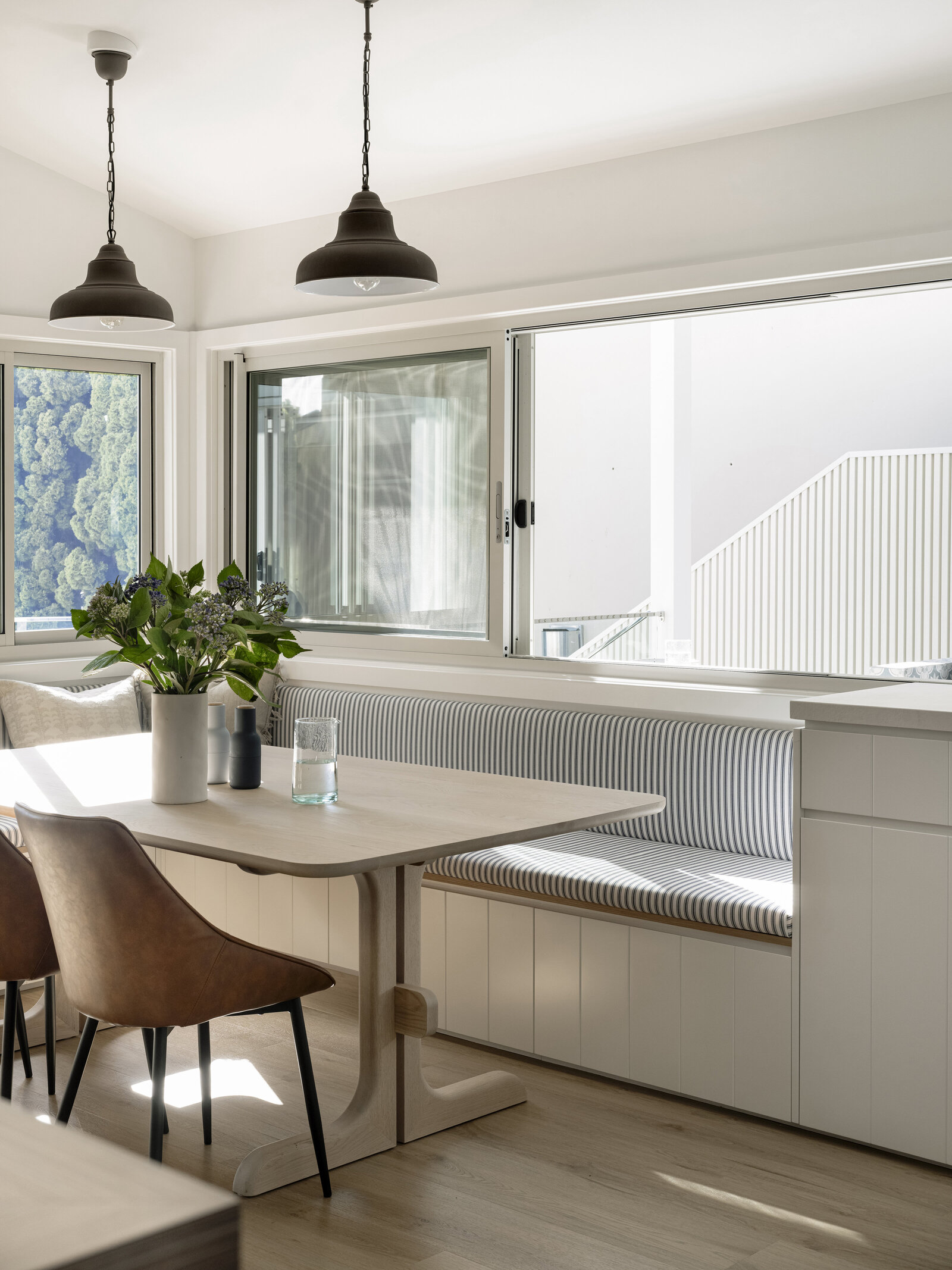 White kitchen cabinets with glass doors and brass handles exude elegance, enhanced by a plant on the left. Discover this exquisite touch in Newcastle Kitchen and Bathroom Designer collections, where style meets functionality.