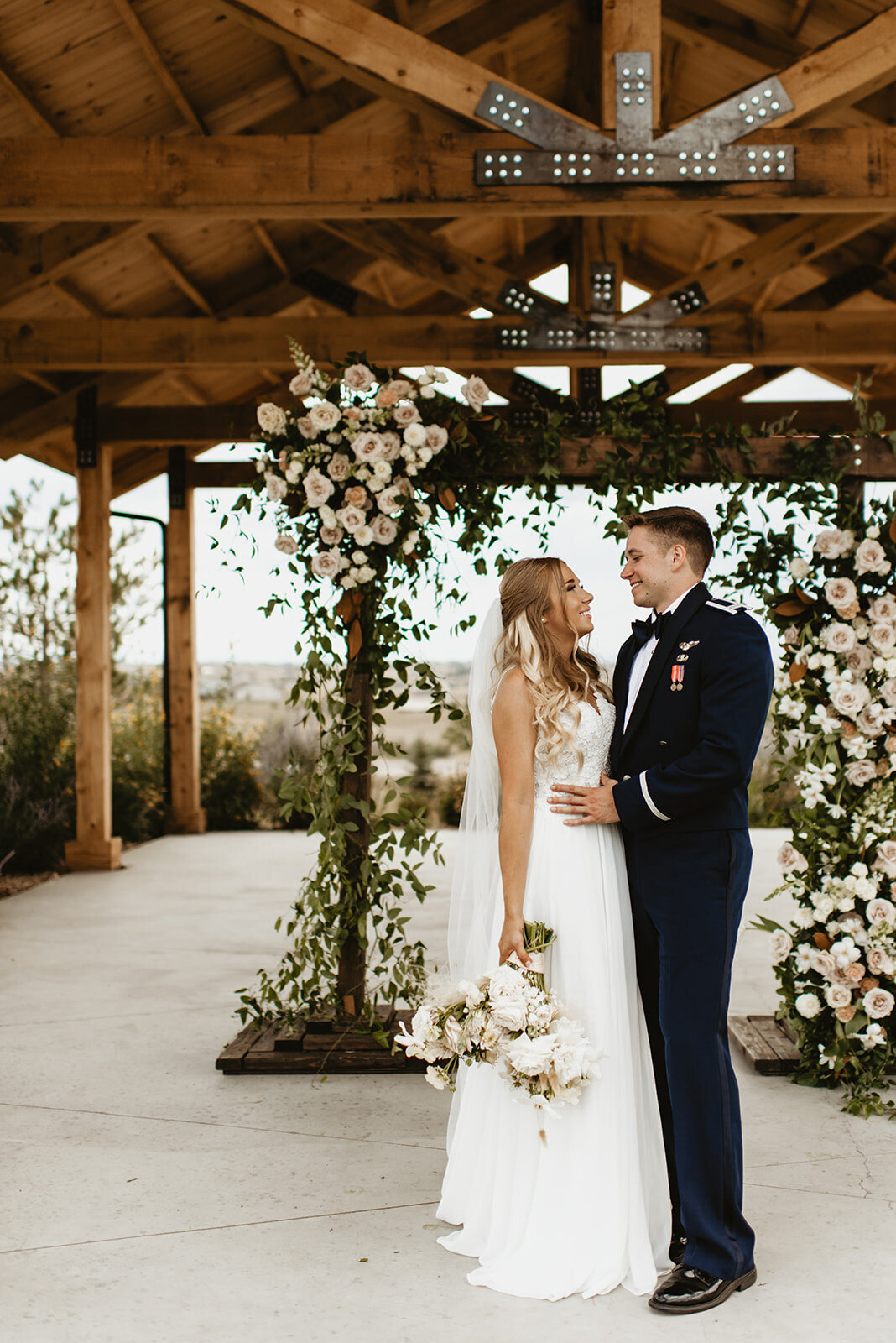 Bride and groom happily facing each other with a an elegant florals behind