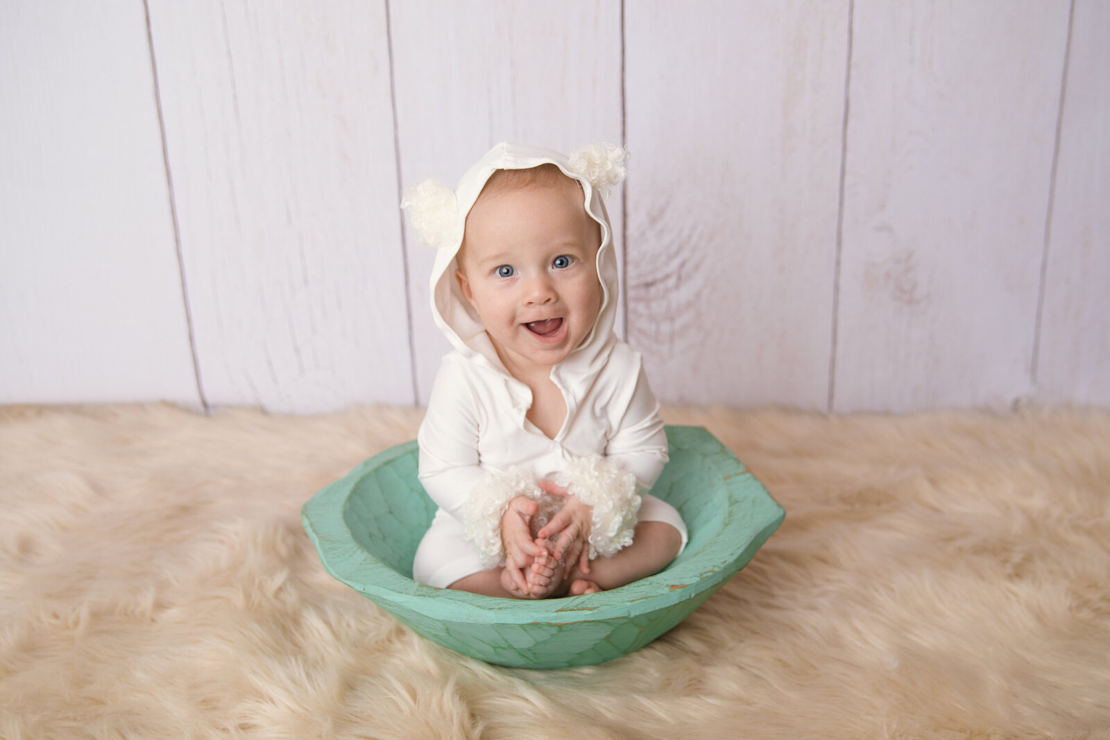 Milestone Photographer, a happy baby smiles while sitting in a wooden bowl