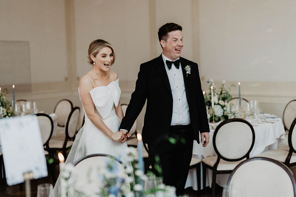 Bride and groom holding hands and smiling looking at their wedding decor by Wednesday Wedding Club