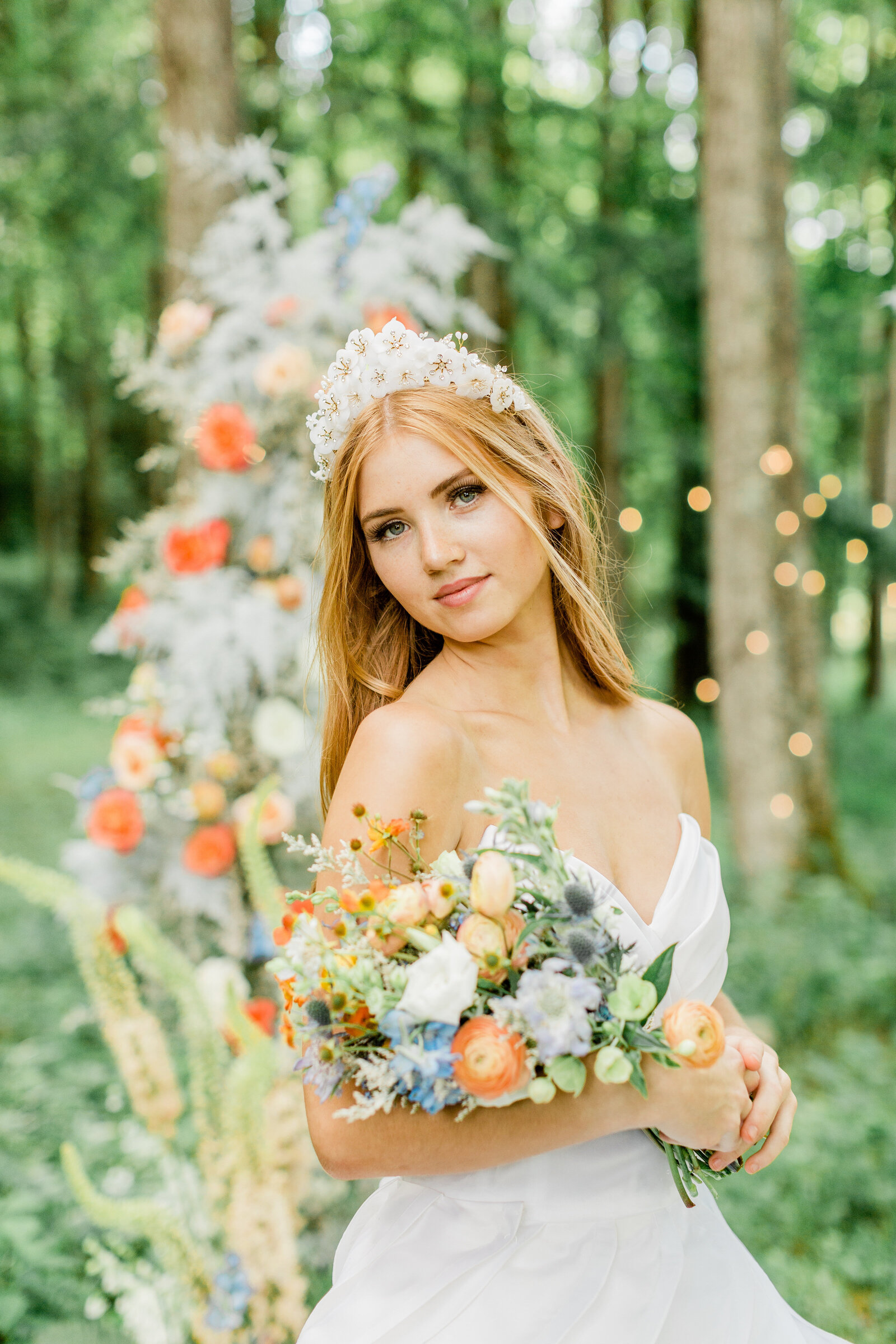 Bridal portrait in Boone, NC of a woman smiling at the camera while wearing a wedding dress and flower crown and holding a bouquet of flowers.