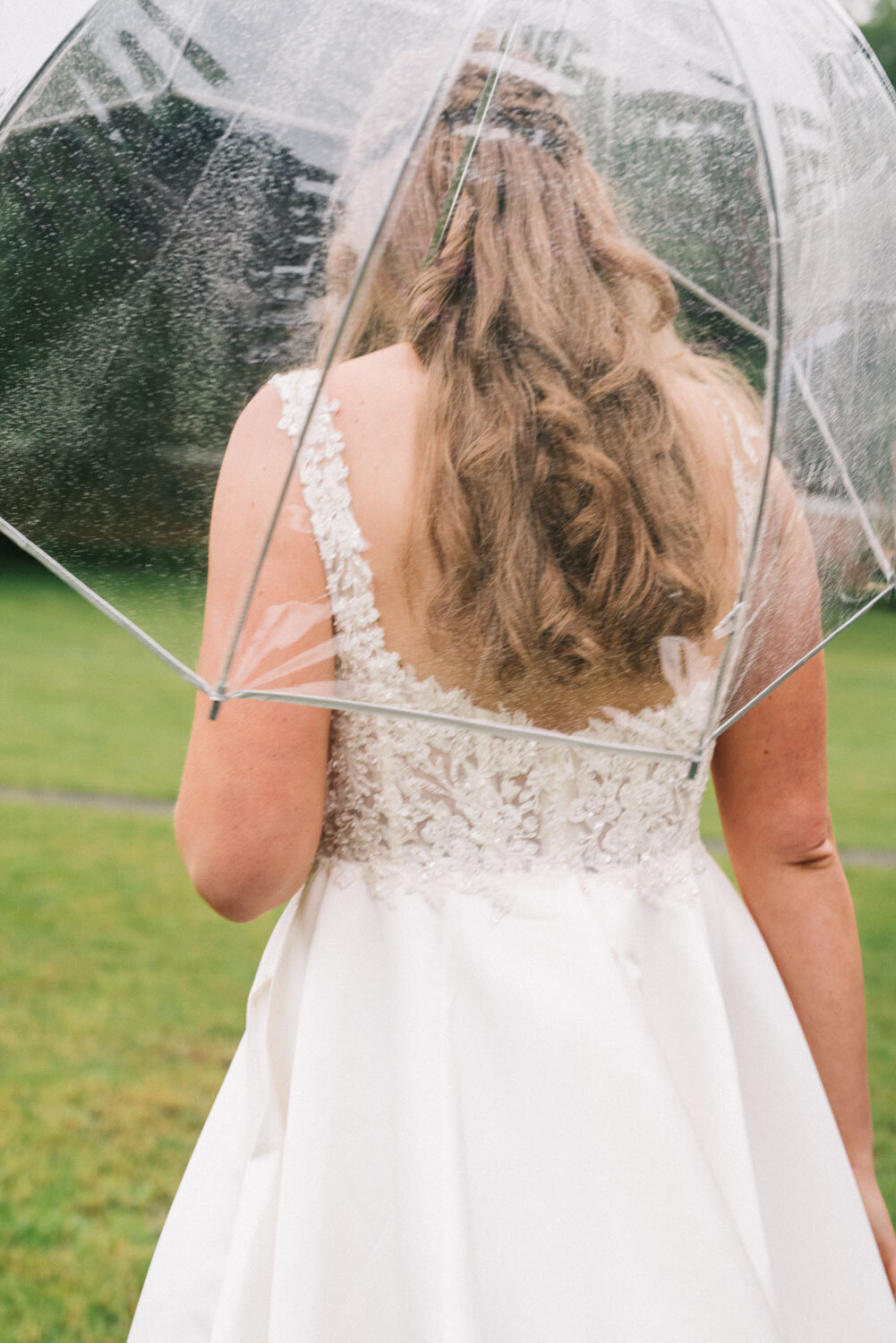 Bride facing backward holding a clear umbrella