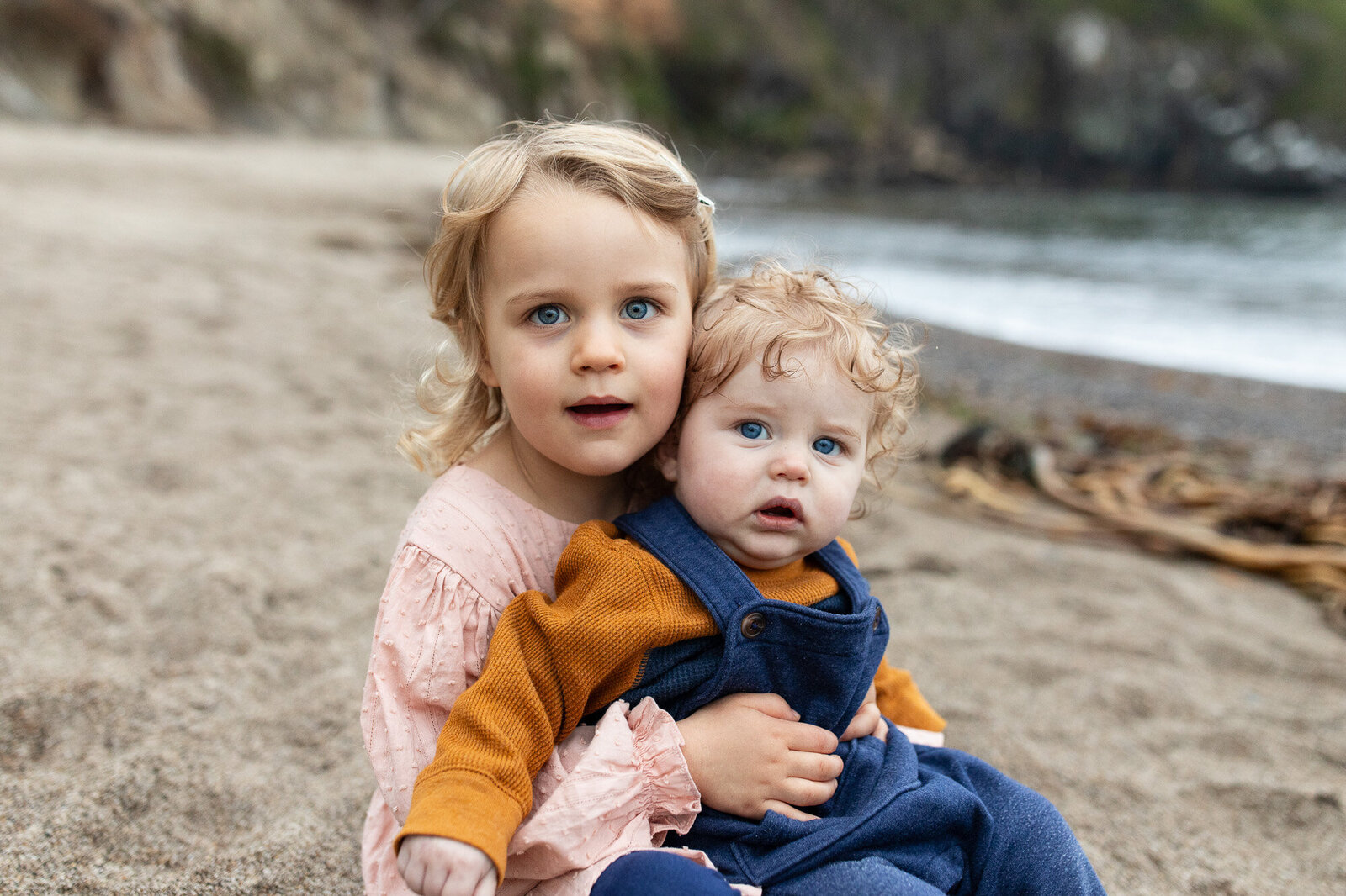 Toddler and infant sitting in the sand  at the oregon coast. Image by Oregon Coast Photographer.