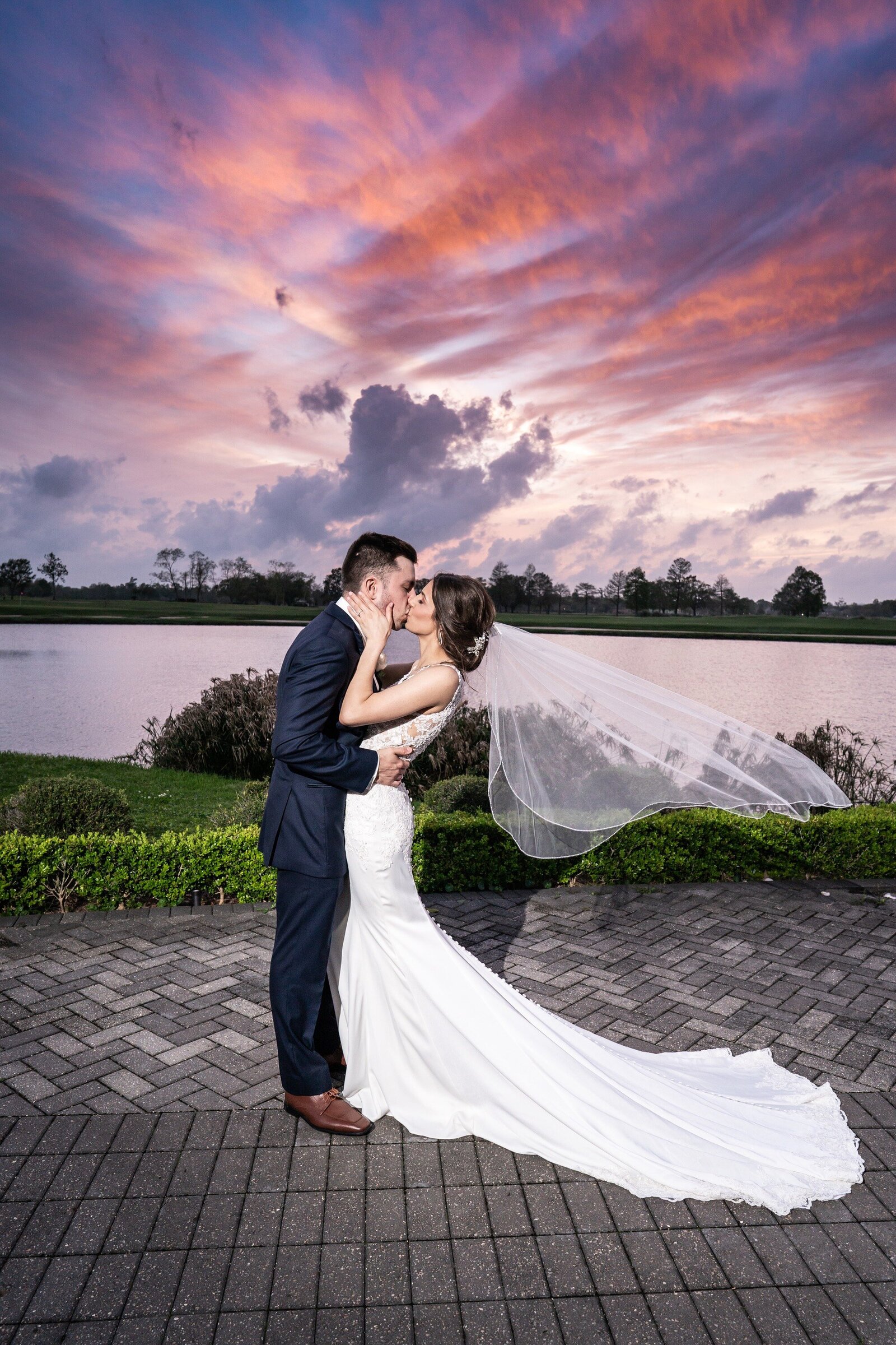 Bride and groom kiss with dramatic sunset behind them at English Turn wedding
