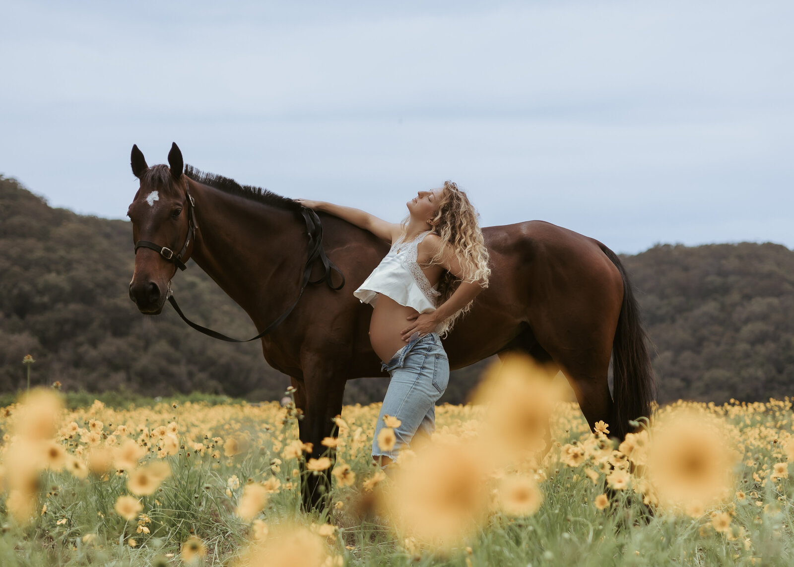The beginning of this mum-to-be's story in a maternity photoshoot with a brown horse, jeans and beautiful yellow flowers.