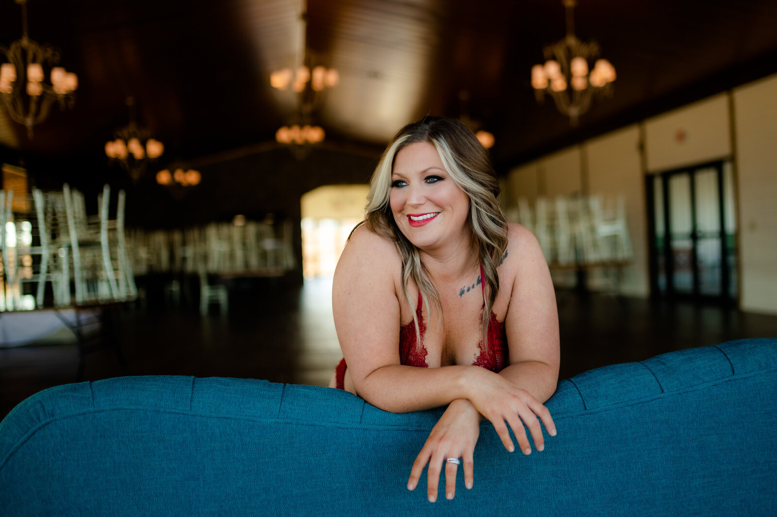 private studio space for Little Rock AR boudoir photography with woman sitting on a blue couch smiling