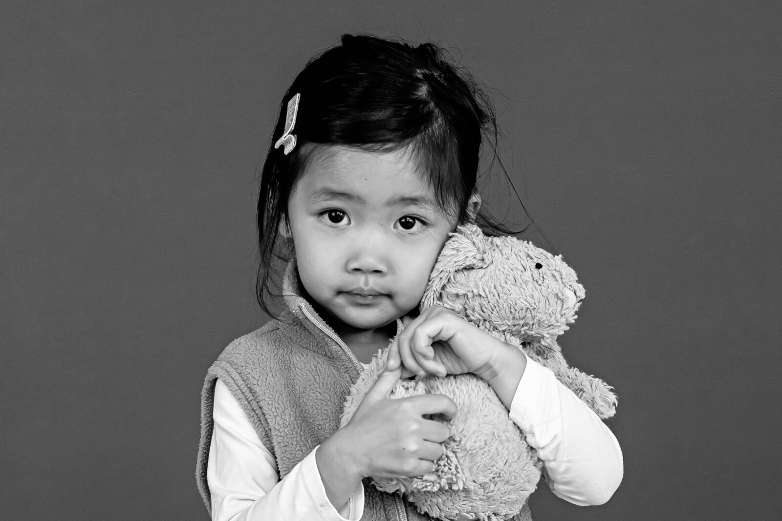 Preschool girl, black and white image, in a ruffle dress with her shoulder shrugged smiling for her school photo.