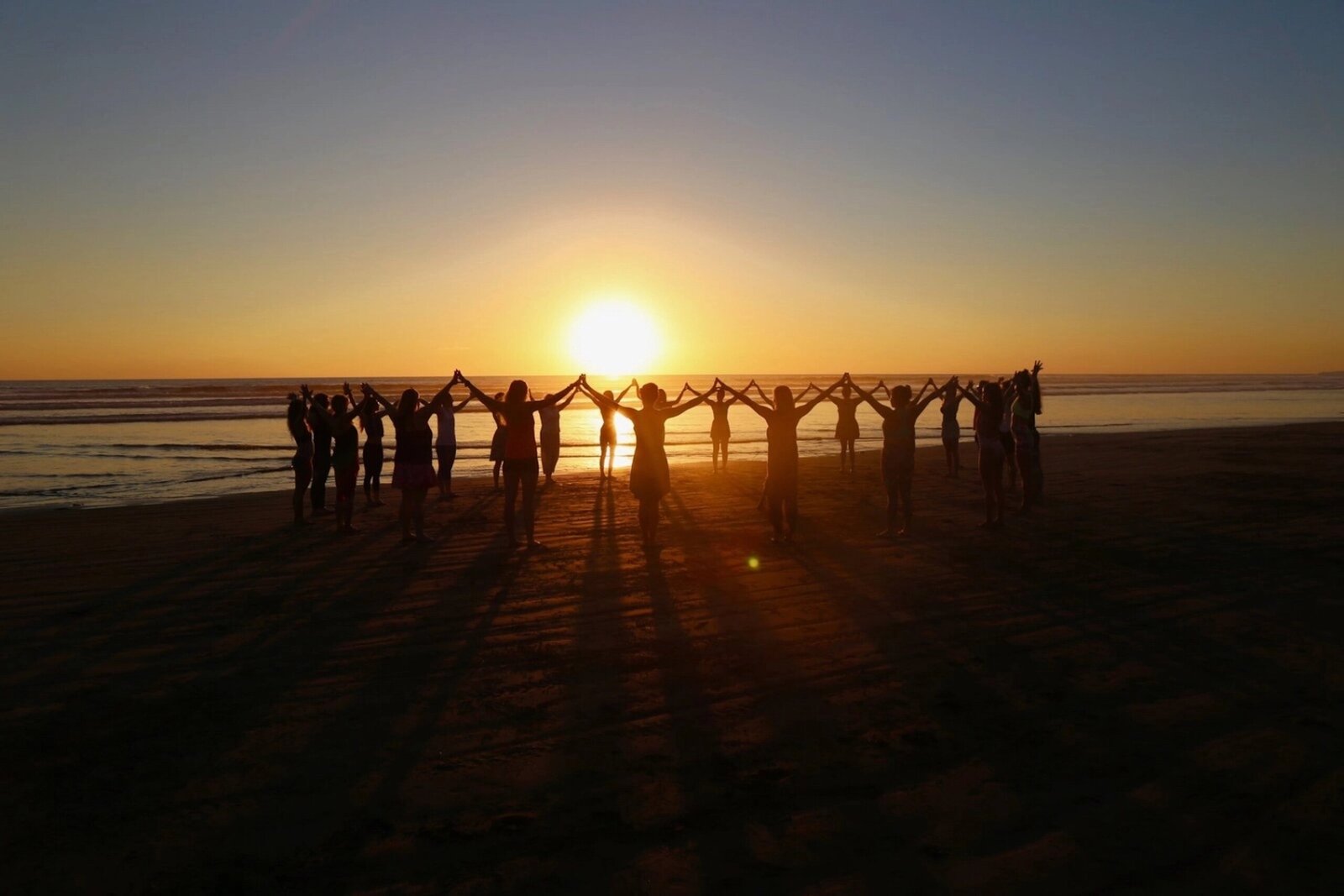 Students holding hands on the beach during Soma Yoga Institute’s yoga teacher training, symbolizing community and transformation.