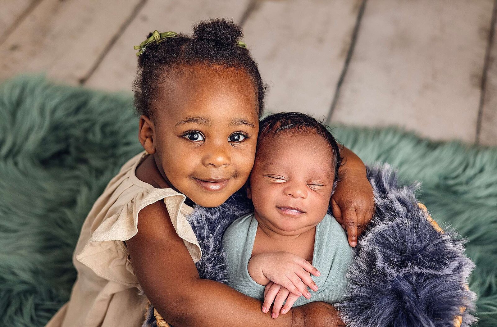 Two children pose happily for a photo, captured by Bia Schaefer Photography during an in-home newborn session.