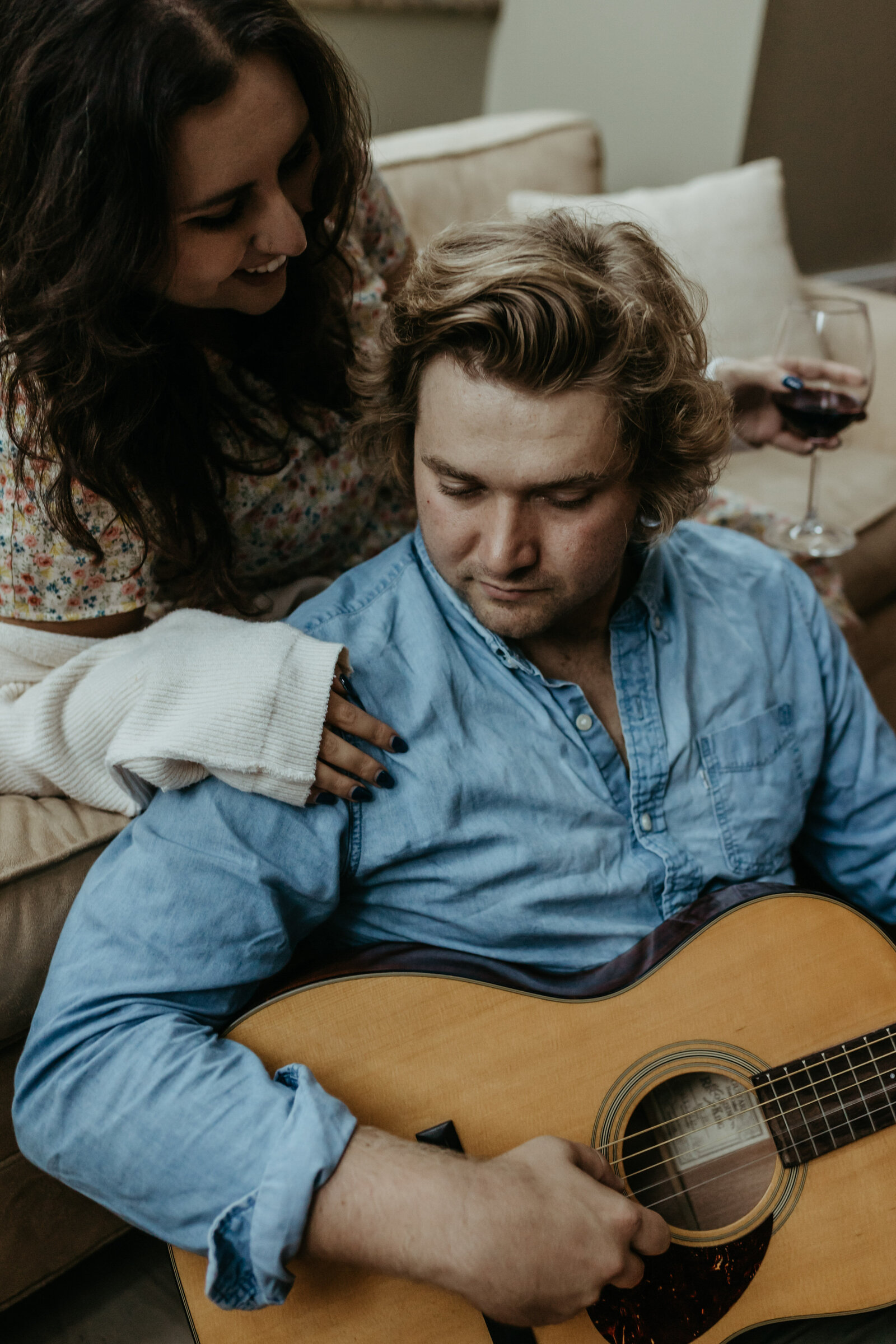 A man and woman sit together with a guitar and wine