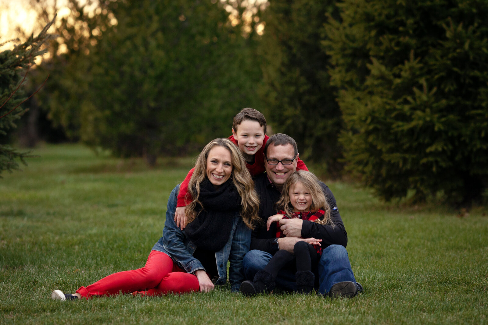 Family of four snuggled close in grass, smiling.