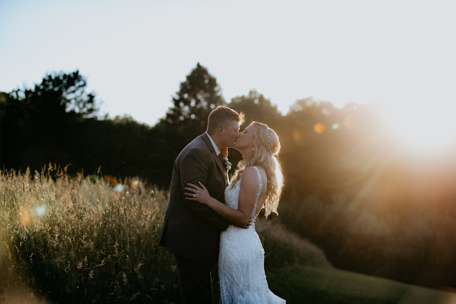 A couple share a romantic kiss during a sunny golden hour after their ceremony.