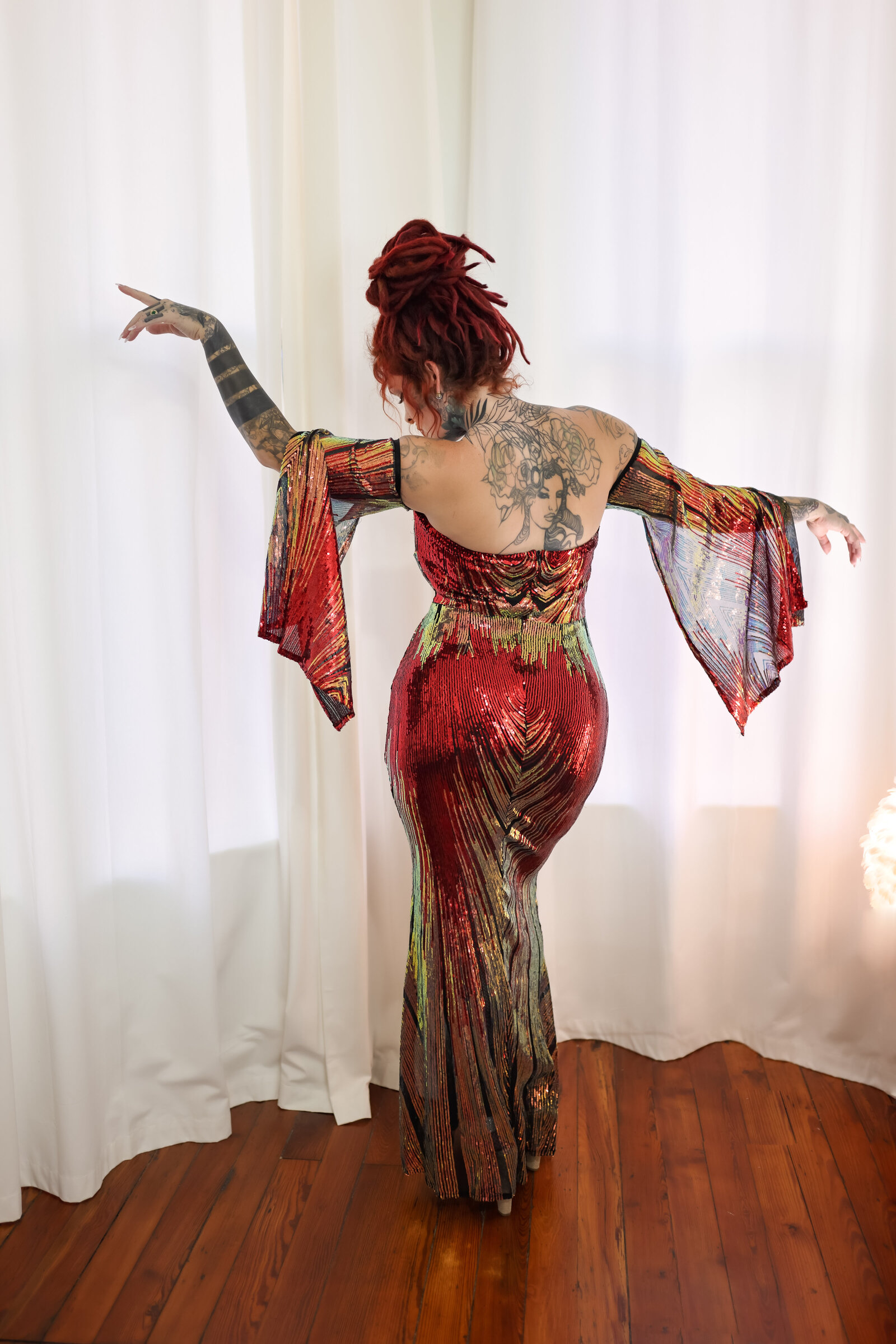 Savannah Boudoir Photography and Glamour showcases gorgeous red headed woman with dreads in colorful and sparkly designer glamour gown in window