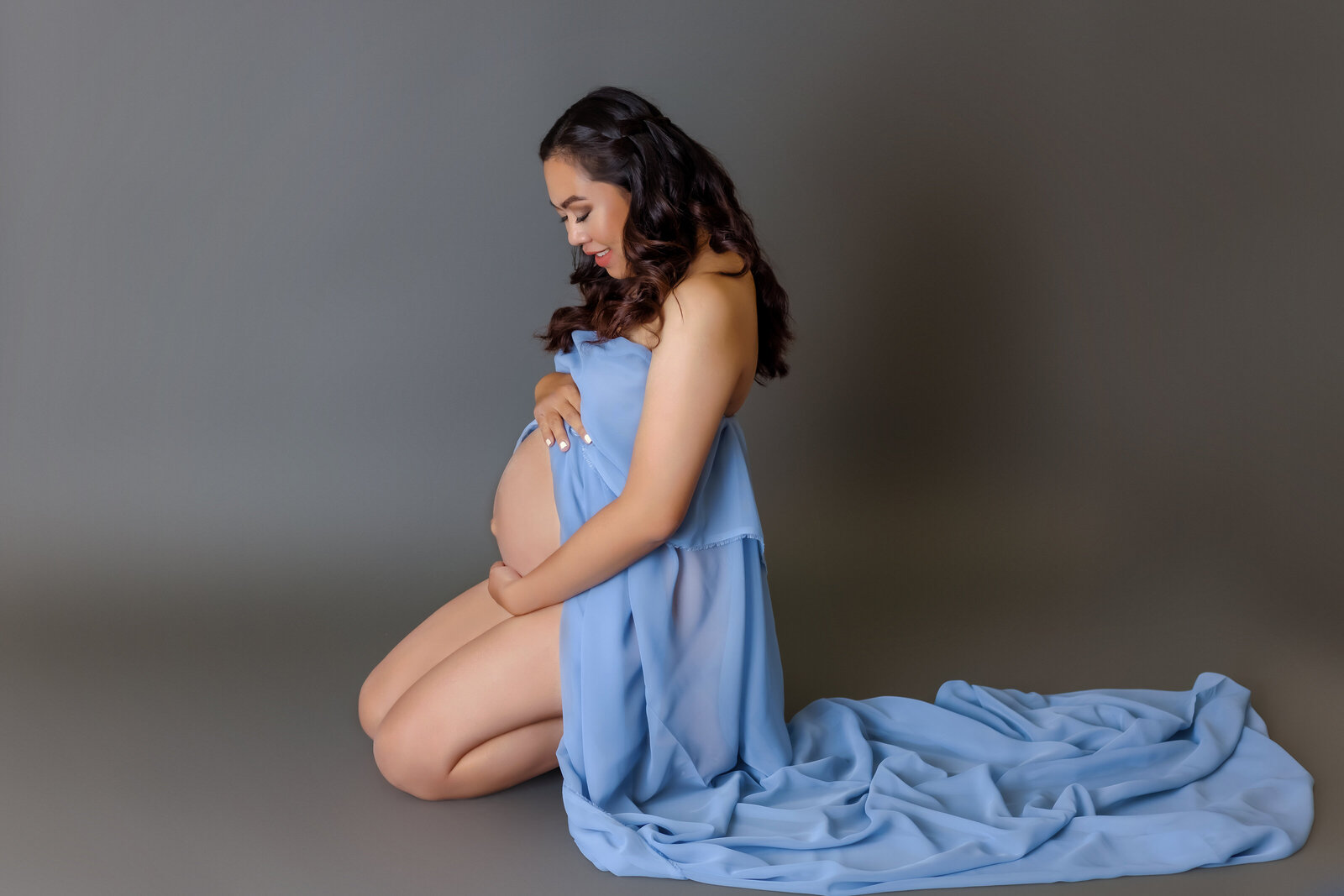 Maternity Photographer, a woman kneels in a pregnancy gown and admires her belly
