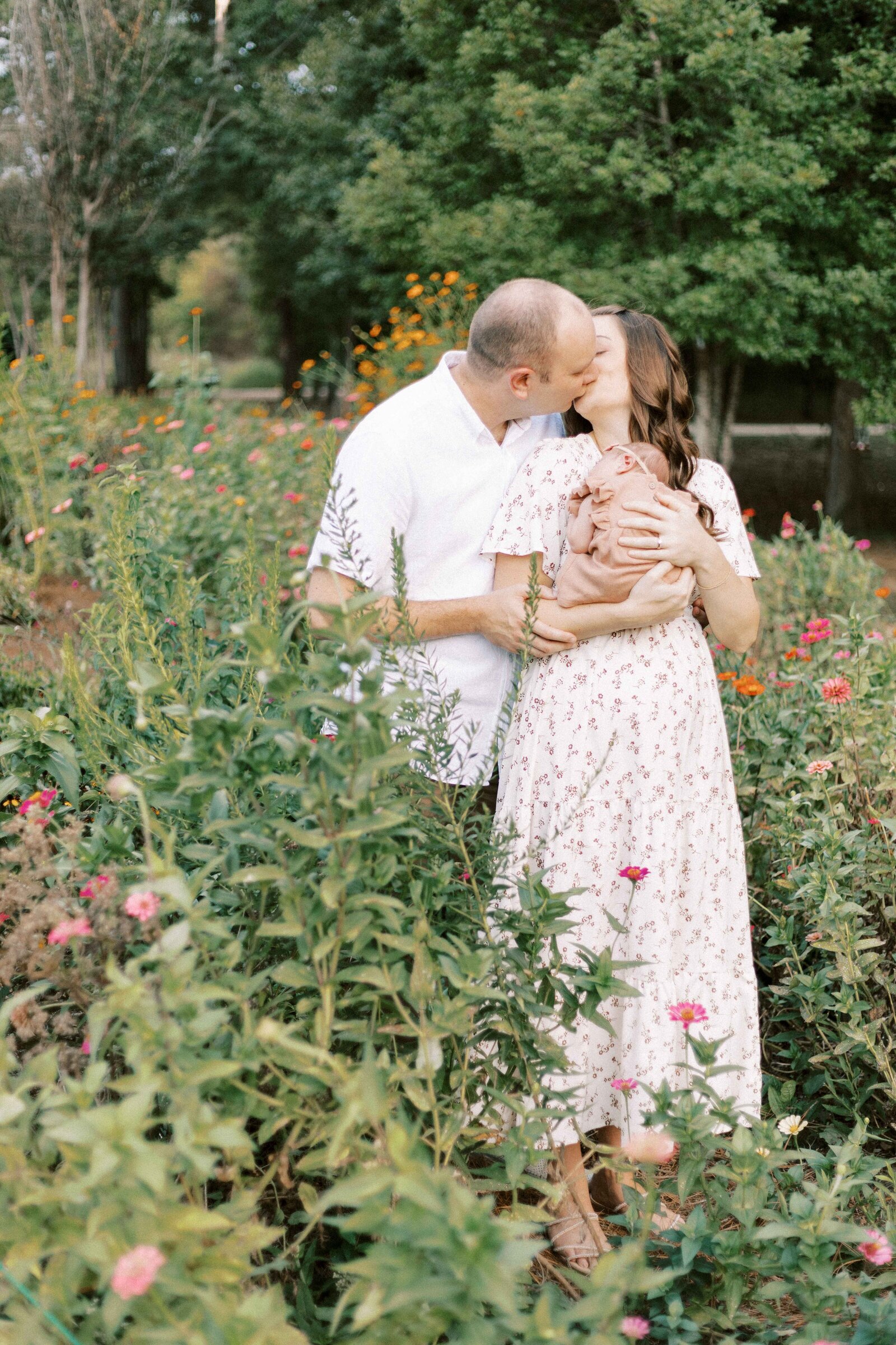 parents kissing in garden while holding baby in peoria illinois newborn photos 