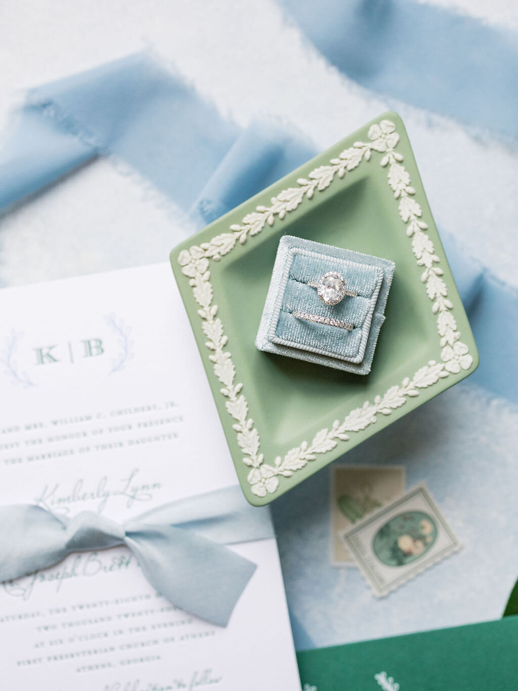 green ring box holding engagement ring on top of blue wedding invitaiations